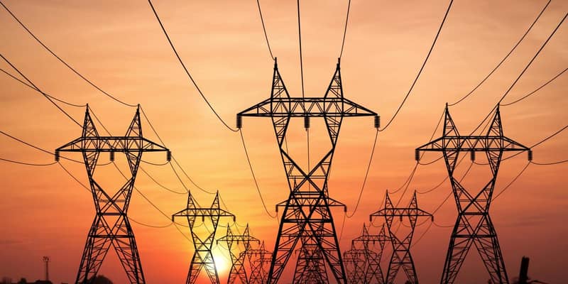 Three rows of electricity pylons against a deep orange sunset sky.