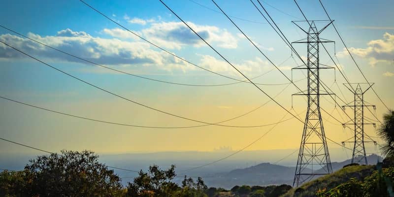 High voltage pylons on a hillside and a city visible in the distant background.