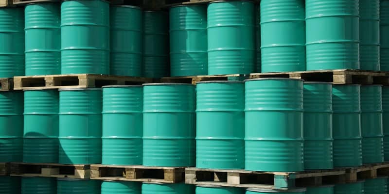 Pile of green industrial barrels stored outside a warehouse.