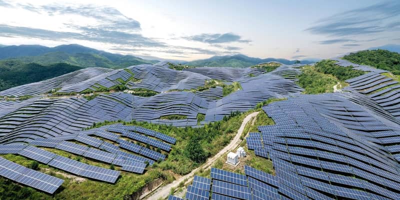 An aerial view of a solar farm, covering many leafy hills.
