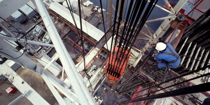 An aerial view of a central column of a drilling rig, with a worker checking the hoist.