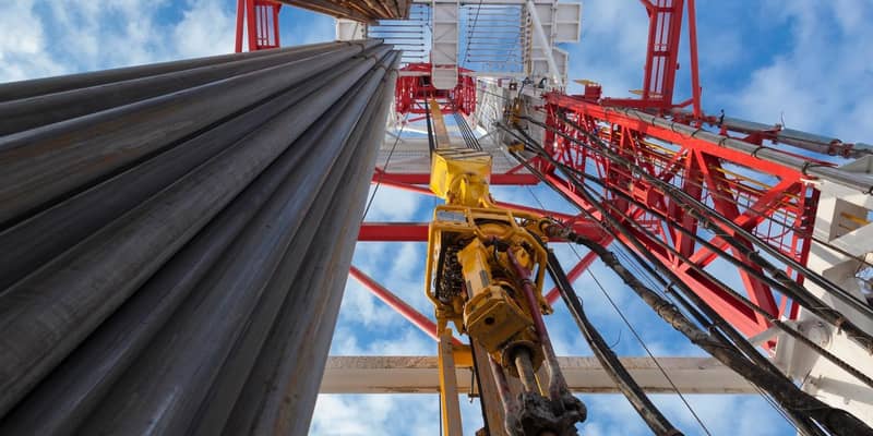 Upward view of a drilling rig with a large pipe and a blue sky.