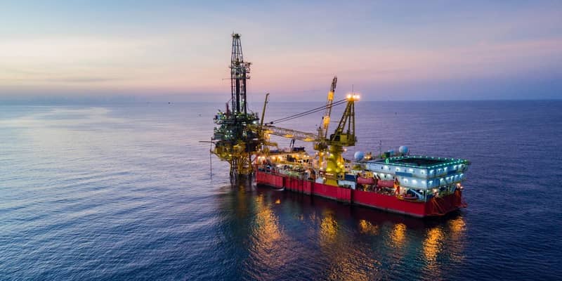 An illuminated oil drilling rig at sea during dusk.