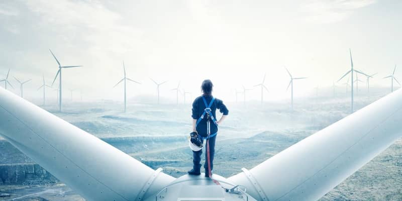 A person standing on top of a wind turbine, looking out at an wind farm, covered in fog.