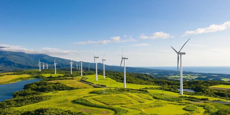 A row of wind turbines in the mountain coastal cliffs, under the blue sky.