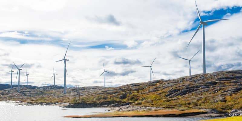Wind turbines across rocky hills, next to a lake.