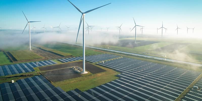 An aerial view of wind turbines and solar panels, in mist countryside fields.