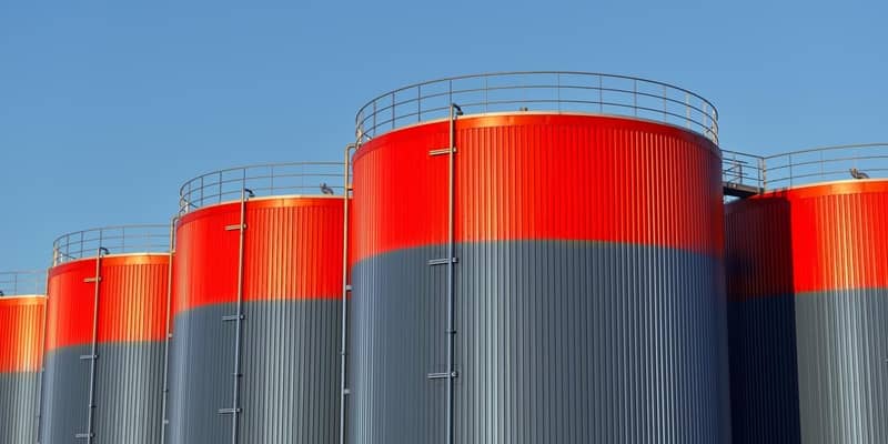 Multiple rows of connected red and grey storage tanks, with a blue sky with copy space in the background.