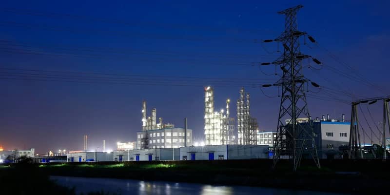 Chemical plant illuminated in the evening, next to a row of electricity pylons.