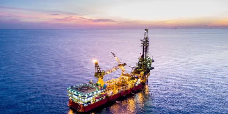 An aerial view of an oil rig in the ocean at sunset, with other rigs in the distance.
