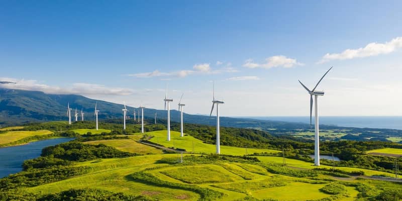 A row of wind turbines in the mountain coastal cliffs, under the blue sky.
