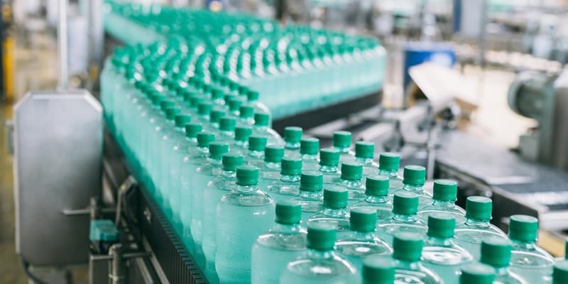 A line of green bottles on a conveyor belt in a factory.