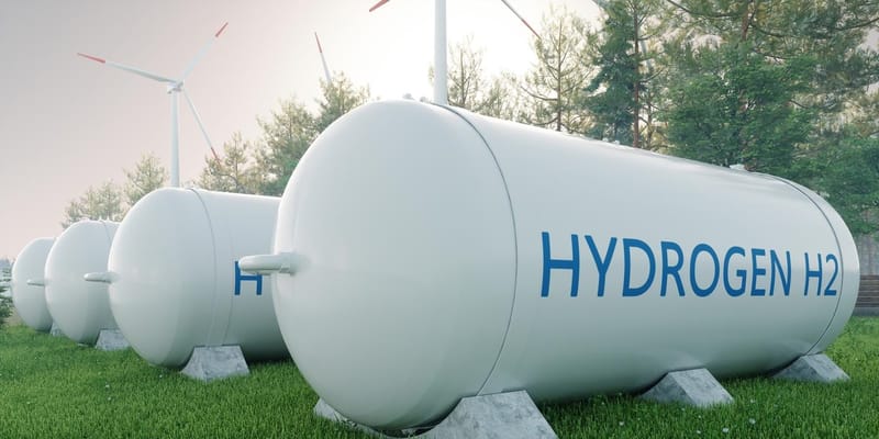 3D render of four hydrogen fuels tanks, in a tree-lined field with wind turbines to the side.