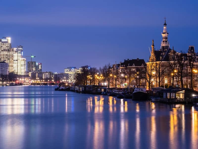 Dawn over the Amstel river where traditional Dutch architecture contrasts with modern office building in Amsterdam, Netherlands