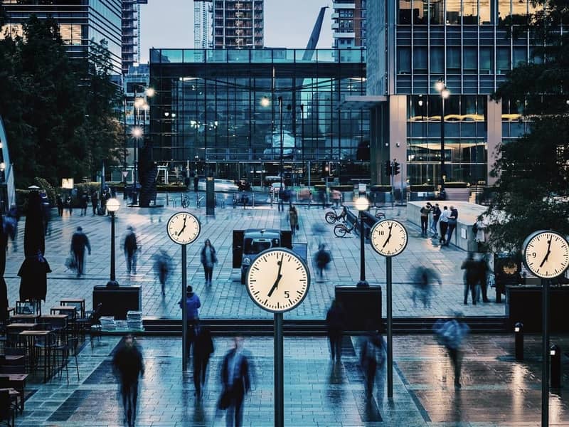 Blurred People walking and clocks in front of Canada Square, Canary Wharf, London.