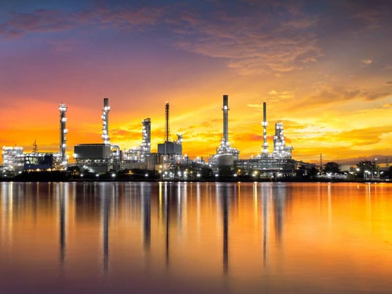A gas refinery during an orange illuminated sunset, with reflection in the water.