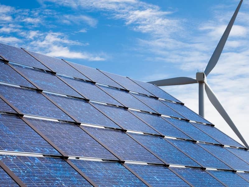 Solar panels and a wind turbine against a blue sky.