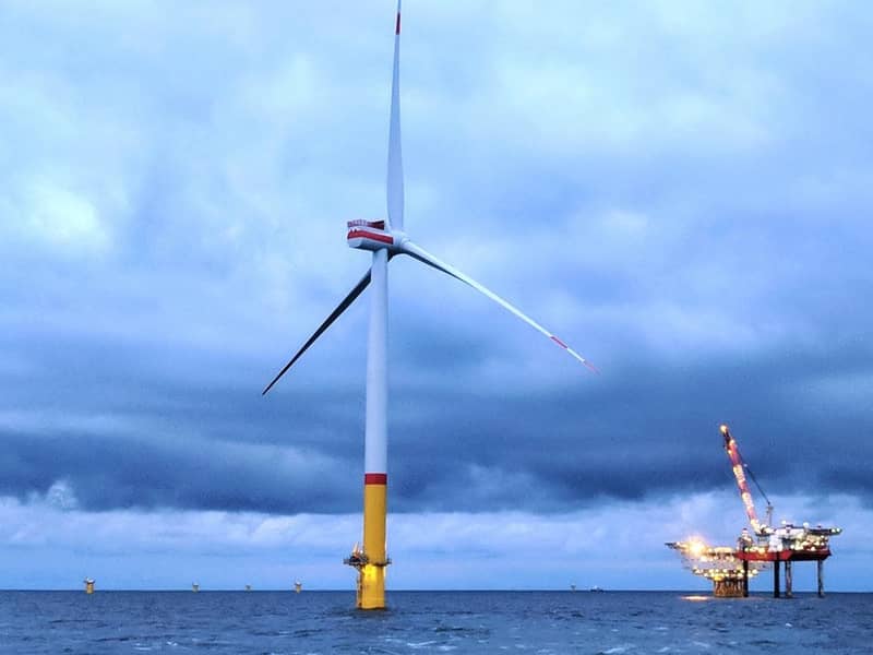 A wind turbine and oil rig in the ocean with a cloudy sky.