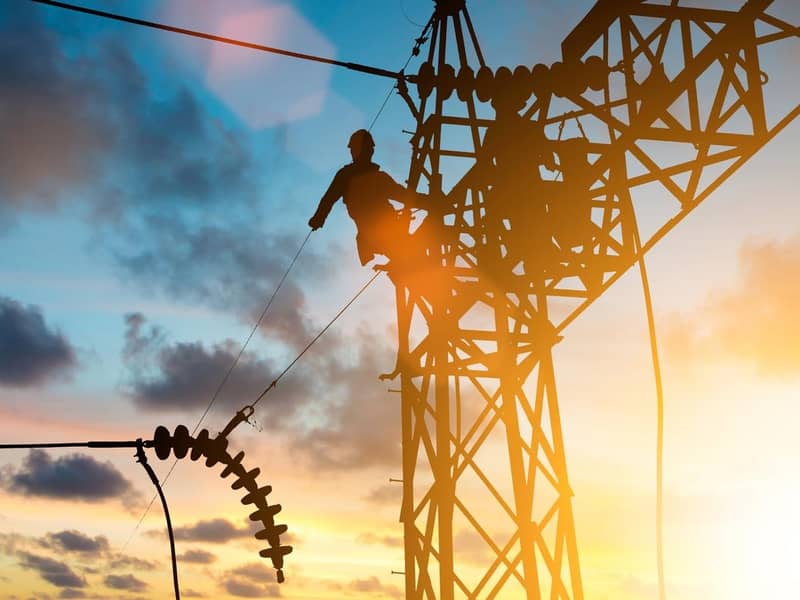 Two men are working on a high voltage power line at sunset.