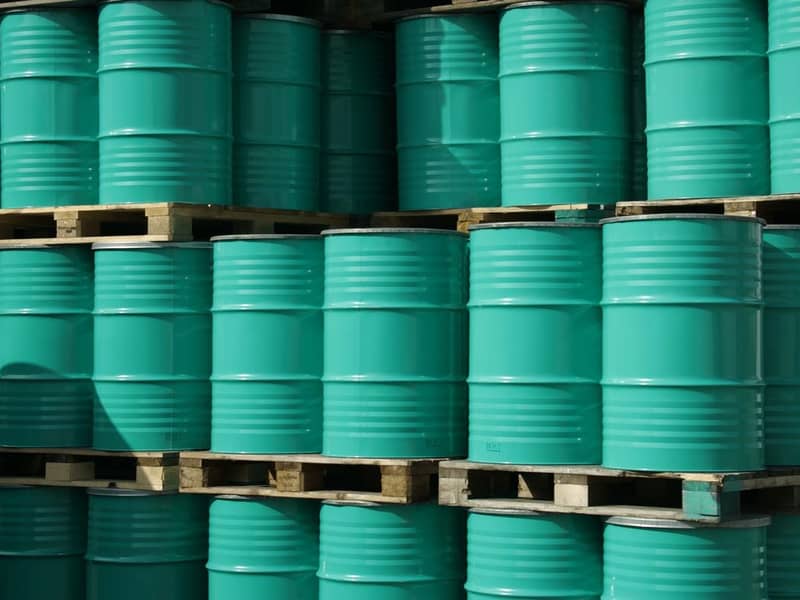 Pile of green industrial barrels stored outside a warehouse.