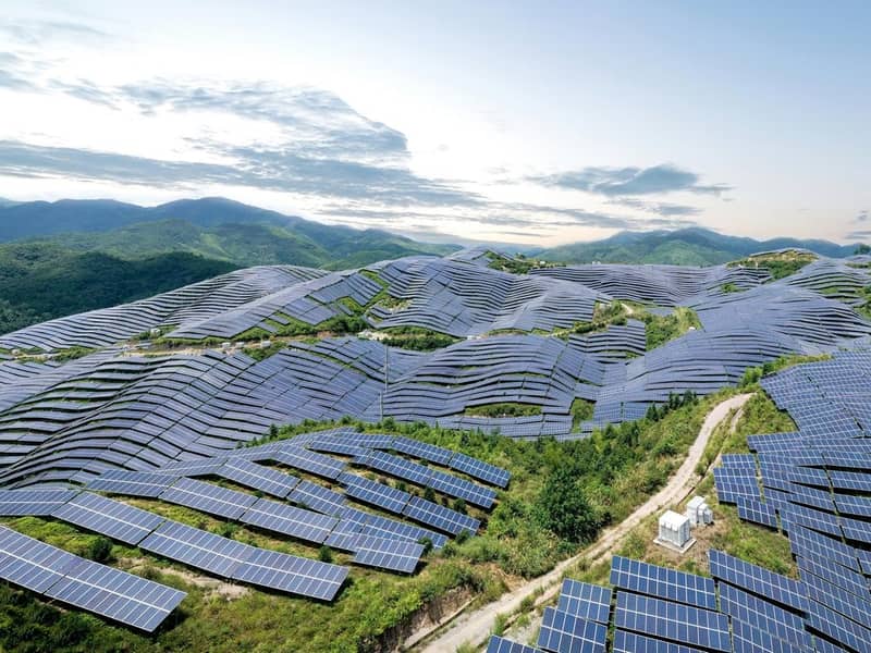An aerial view of a solar farm, covering many leafy hills.