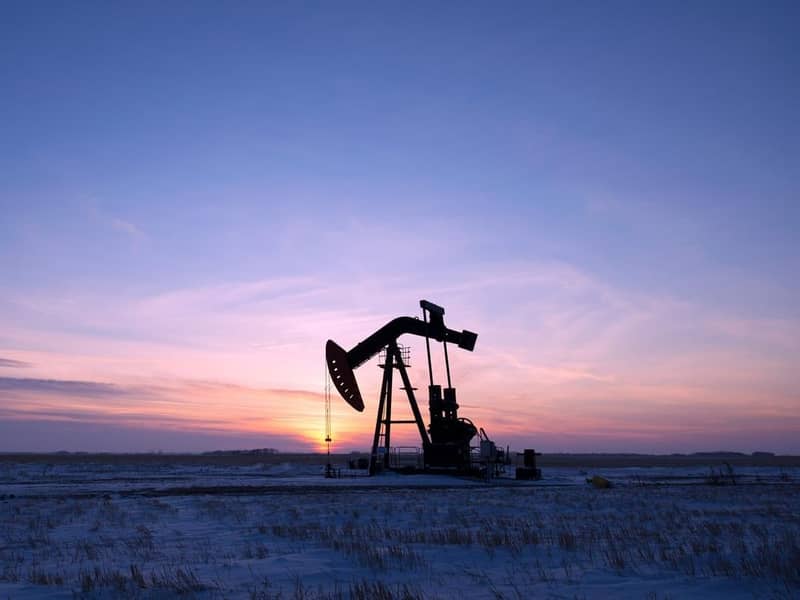 An oil pump in a vast snow covered field at sunset.