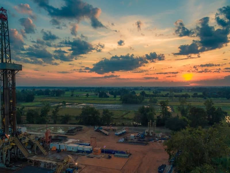 An aerial view of a drilling rig, in country fields at sunset.