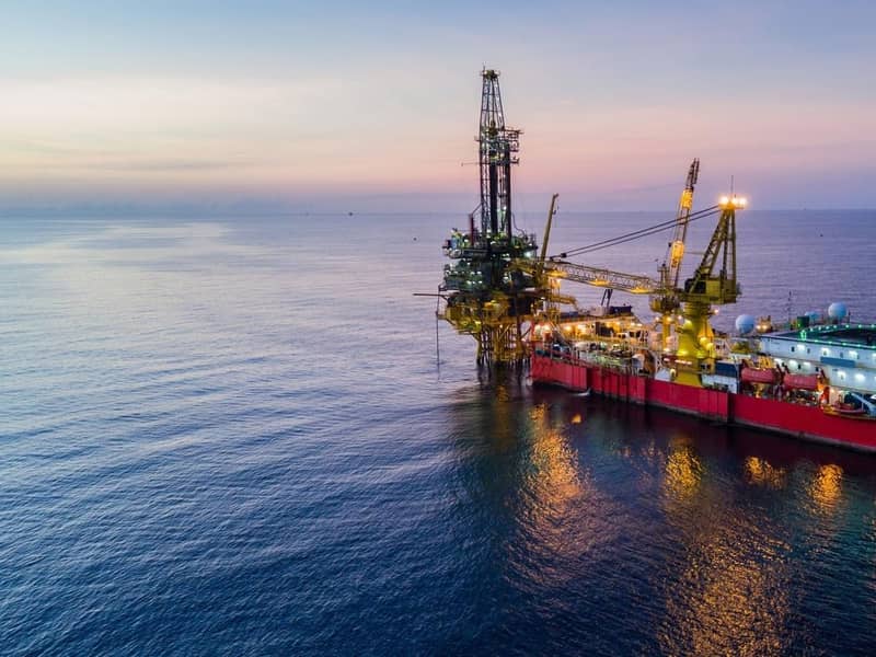 An illuminated oil drilling rig at sea during dusk.