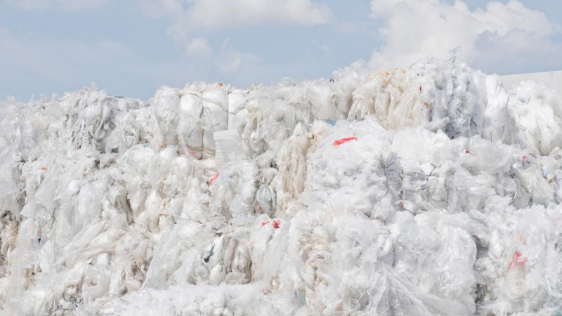 A pile of plastic bags on the ground, with a cloudy blue sky in the background.