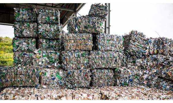 Multiple stacked bales of plastic waste, in an open-sided warehouse.