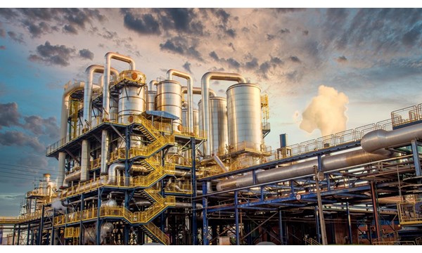 The exterior of a large industrial plant with blue and yellow railings. External stairwells, multiple pipes and large cylinders.