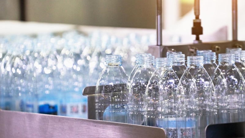 Several batches of empty white plastic bottles, being processed on a conveyor belt.