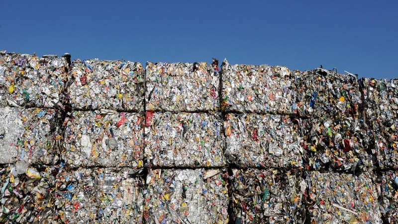 Multiple bales of plastic waste, piled high with a blue sky in the background.