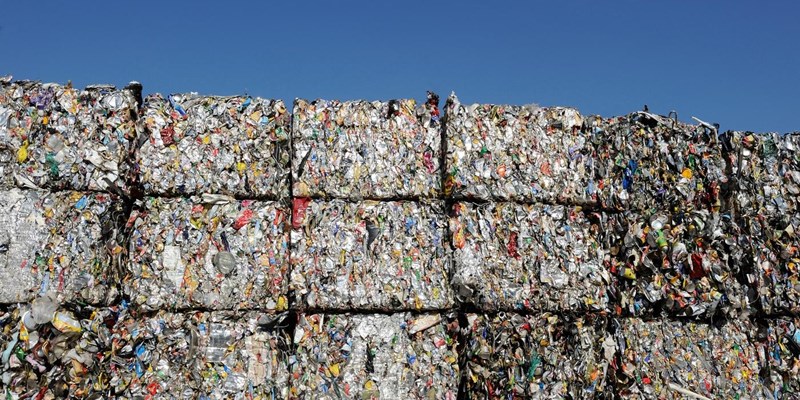 Multiple bales of plastic waste, piled high with a blue sky in the background.
