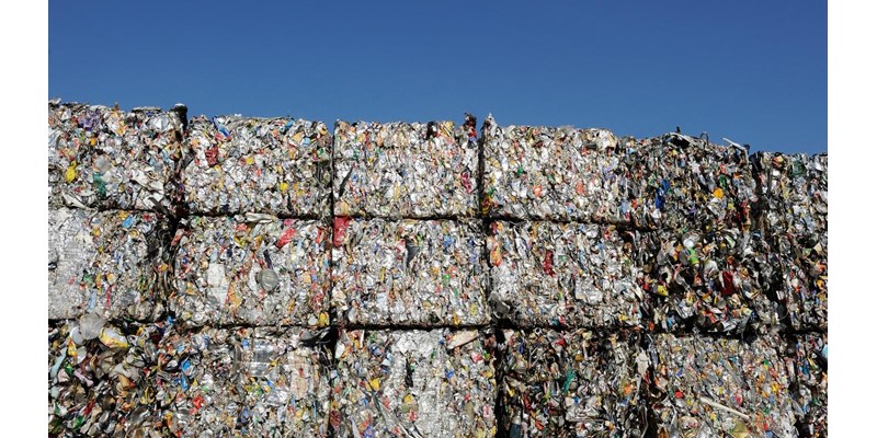 Multiple bales of plastic waste, piled high with a blue sky in the background.