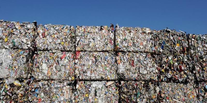 Multiple bales of plastic waste, piled high with a blue sky in the background.
