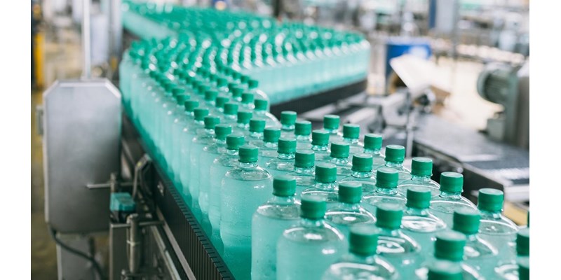 A line of green bottles on a conveyor belt in a factory.