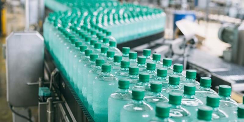 A line of green bottles on a conveyor belt in a factory.