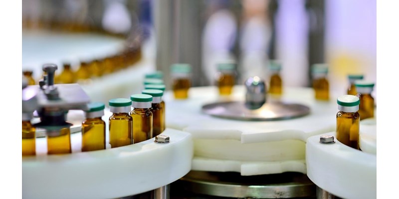 A close-up of a machine making medicine bottles on a conveyor belt, in a factory.