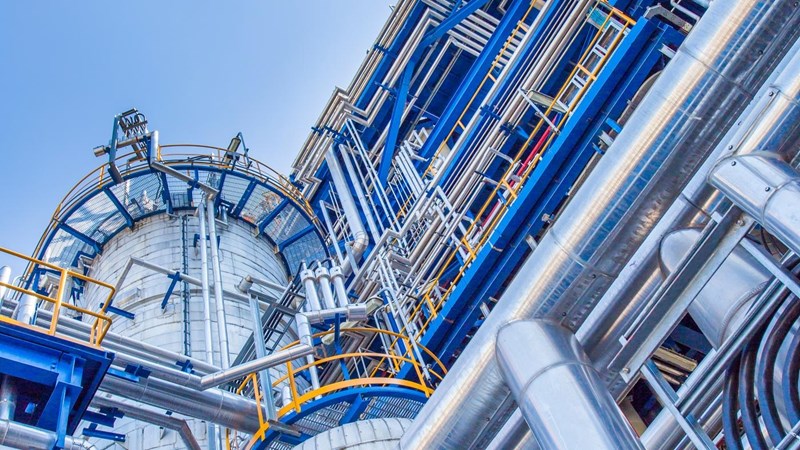The exterior of an industrial plant with blue and yellow platforms, around a large metal cylindrical tank.