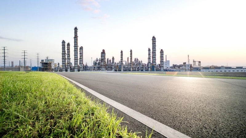 A road in front of an oil refinery, showing pylons to the left side in the distance.