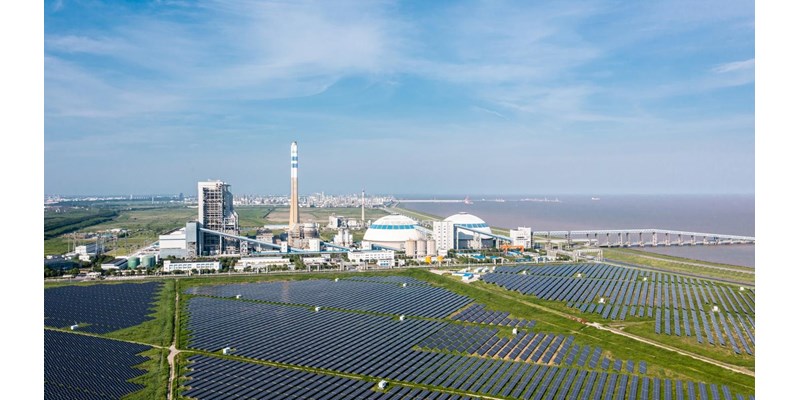 An aerial view of a solar power plant on a coastline, next to the sea and blue skies.