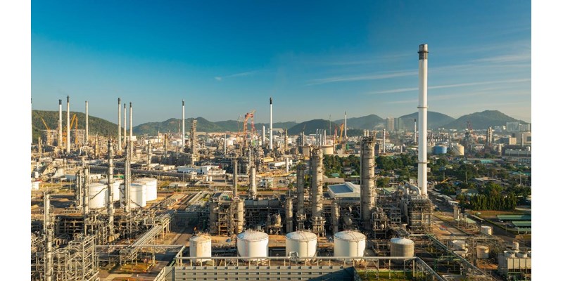 An aerial view of an oil refinery with mountains and clear blue skies in the background.