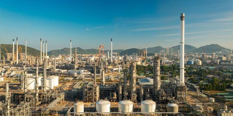 An aerial view of an oil refinery with mountains and clear blue skies in the background.
