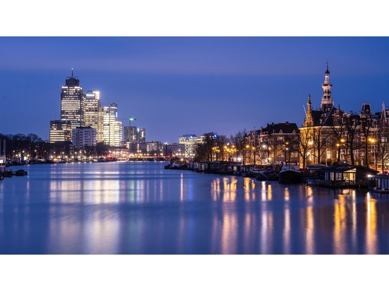 Dawn over the Amstel river where traditional Dutch architecture contrasts with modern office building in Amsterdam, Netherlands