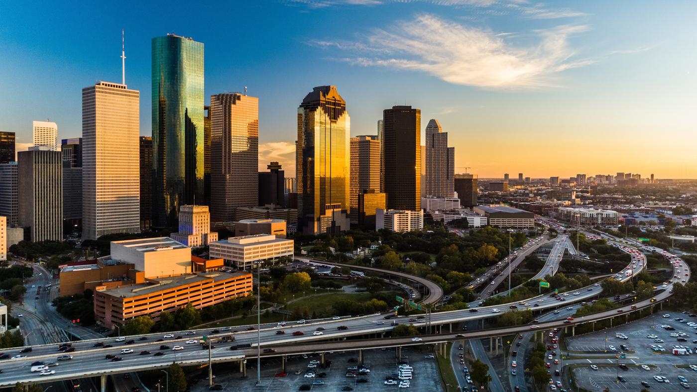 Downtown Houston skyline aerial at sunset with a highway in the foreground, angled view with the Texas Medical Center in the far distance