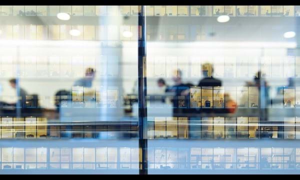 Workers working late. Tall building reflected by lights on the glass facade.