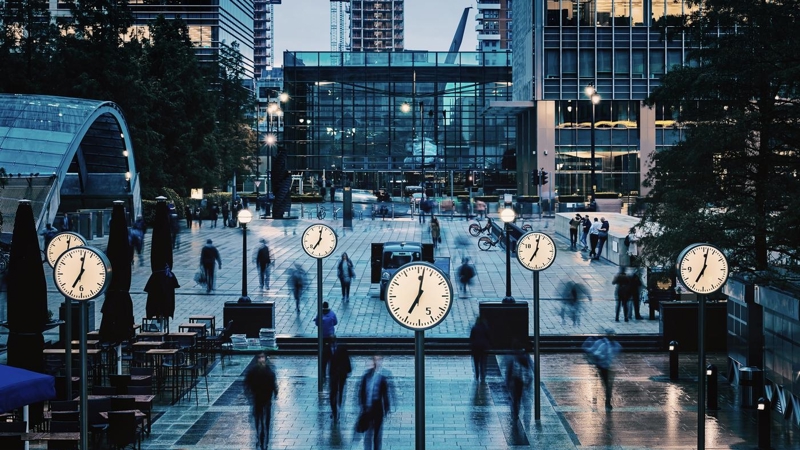 Blurred People walking and clocks in front of Canada Square, Canary Wharf, London.