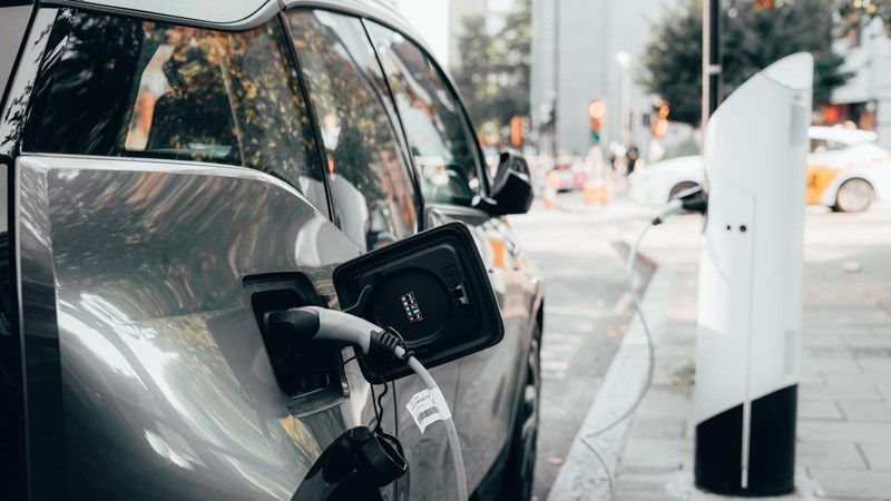 Car parked a busy urban street, plugged into an electric vehicle charging station.