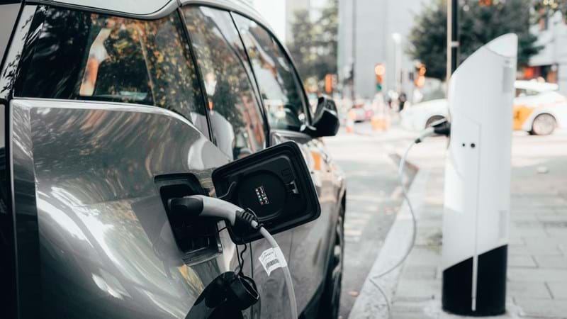 Car parked a busy urban street, plugged into an electric vehicle charging station.